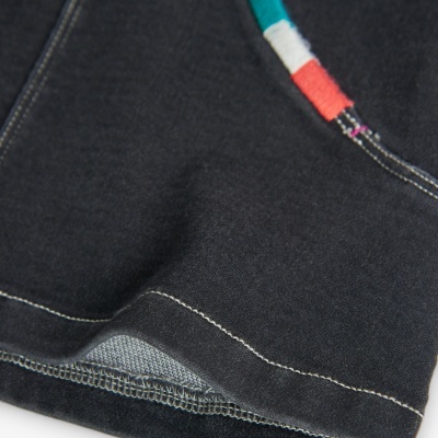 Detalhe de peça de vestuário preta com costuras claras e detalhe colorido