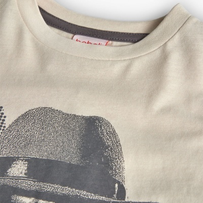 Camisola bege com estampa cinza de chapéu e etiqueta vermelha interior.