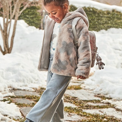 Criança com casaco felpudo camuflado e mochila rosa numa paisagem com neve