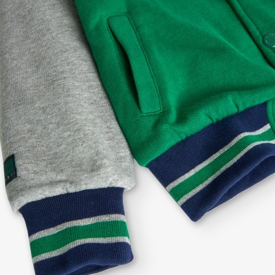 Detalhe de manga cinzenta e parte verde de casaco com punhos canelados e bolso