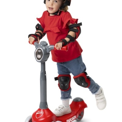 Criança com capacete e equipamentos de proteção a andar num trotinetes vermelho Ducati.