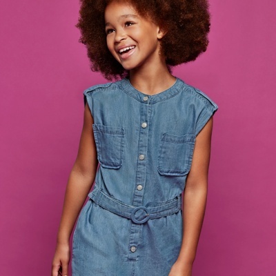 Criança com macacão curto de ganga azul com botões prateados e cinto