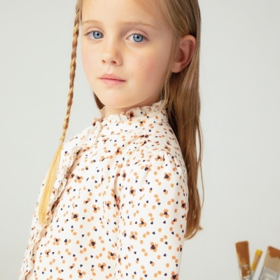 Menina loira com blusa estampada branca de manga comprida e gola franzida