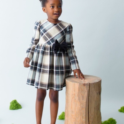 Menina com vestido xadrez e sapatos rosa ao lado de tronco de madeira