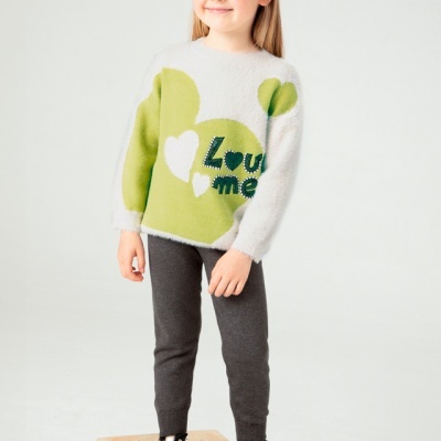 Criança vestindo camisola de malha branca e verde com corações e texto, calças cinza e ténis pretos