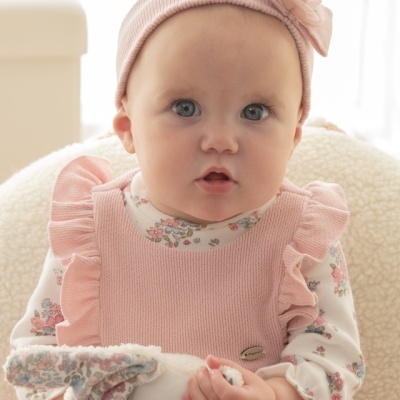 Bébé com vestido rosa e faixa de cabelo sentada numa cadeira clara segurando brinquedo macio