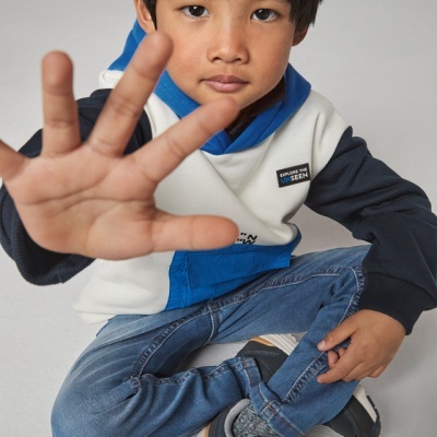 Criança com roupa casual colorida e sapatos pretos sentada no chão com a mão estendida para a frente