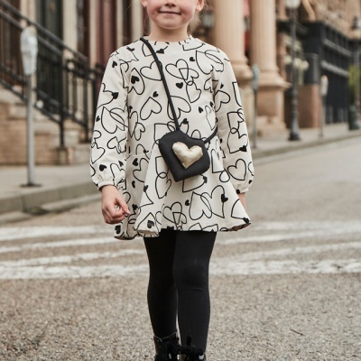 Criança com vestido branco de corações pretos e bolsa pequena preta com coração dourado