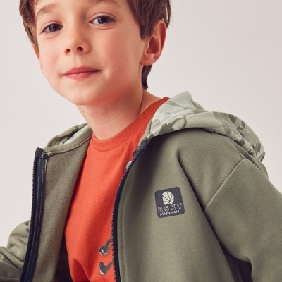 Criança com casaco verde-oliva com capuz e t-shirt laranja