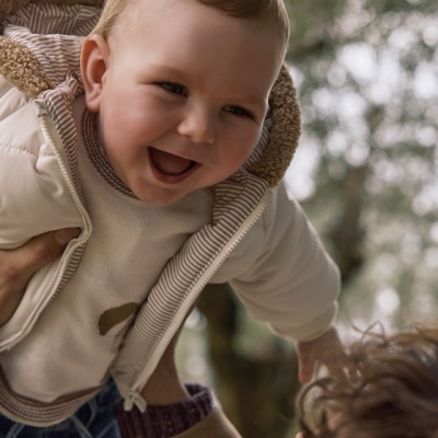bebé sorridente com casaco bege e camisola creme ao ar livre
