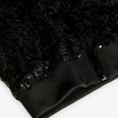 Detalhe de peça de roupa preta com lantejoulas e fecho