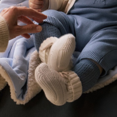 Bebé vestido com calças e meias de malha azul e branca sentado numa manta azul clara