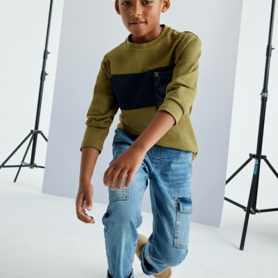Menino com camisola verde-oliva e calças de ganga azuis num estúdio fotográfico