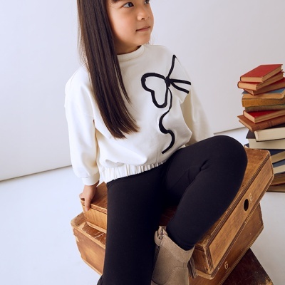 Criança com roupa casual branca e preta sentada em caixas de madeira junto a livros