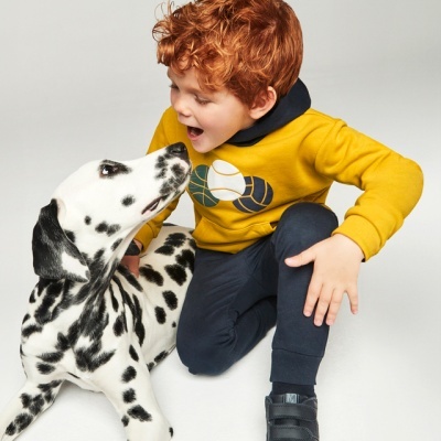 Menino ruivo com casaco amarelo e sapatilhas pretas com cão dálmata preto e branco