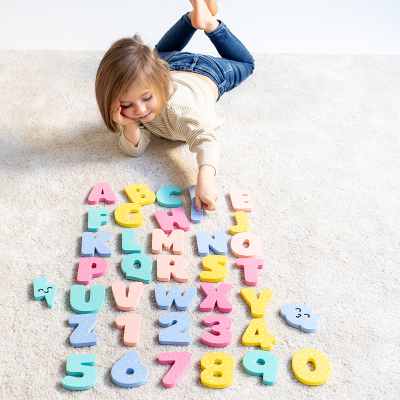 Criança deitada com letras e números de espuma coloridos num tapete claro