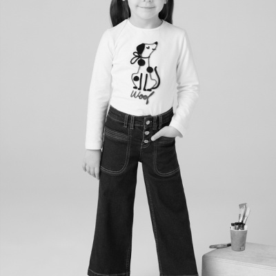 criança com camisola branca e calças de ganga pretas em fundo cinzento claro