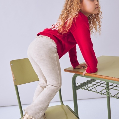 Criança em roupa vermelha e bege em cadeira verde junto a mesa