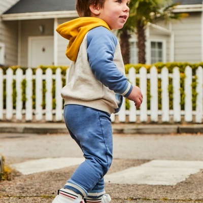 Criança com roupa colorida e ténis brancos numa rua em frente a casa