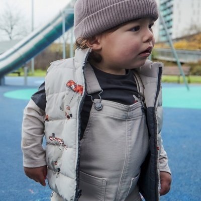 Criança com roupa casual e colete acolchoado a brincar num parque urbano