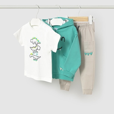 Conjunto infantil com t-shirt branca de dinossauros, casaco verde água e calças bege pendurados