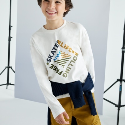 Camisola branca de manga comprida com texto e criança com casaco azul e calças castanhas