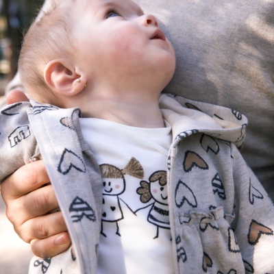 Bebé com casaco cinza de corações e T-shirt branca com desenho de crianças sorridentes.