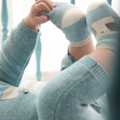 Roupa de bebé azul clara em malha, com padrão branco e meias, num berço azul.