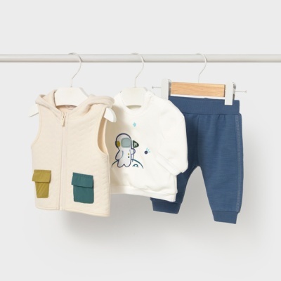 Conjunto infantil com colete bege, camisola branca com astronauta e calças azuis pendurados