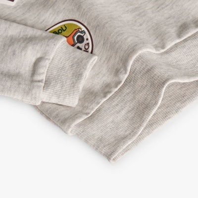 Manga e parte inferior de peça de roupa cinzenta com patch redondo de desenho e texto parcial