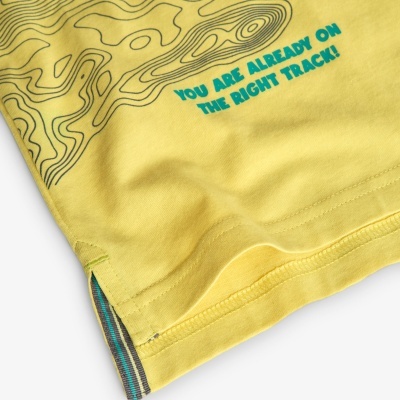 Detalhe da parte inferior de uma peça de roupa amarela com texto azul e padrões negros.