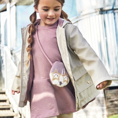 Criança com vestido rosa, casaco bege, mochila de raposa e faixa de cabelo rosa ao ar livre