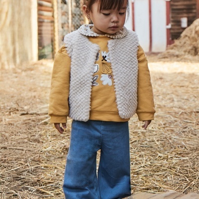 Criança com casaco amarelo, colete bege e calças azuis ao ar livre junto a uma tartaruga