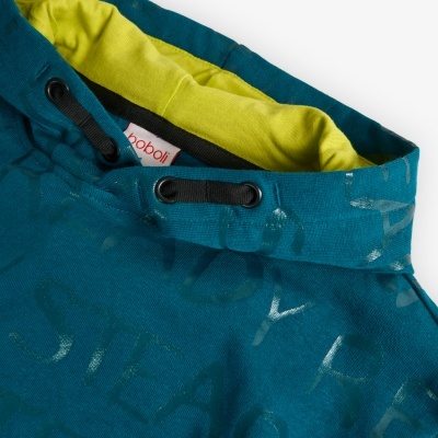 Detalhe de casaco azul petróleo com interior amarelo e padrão de letras prateadas