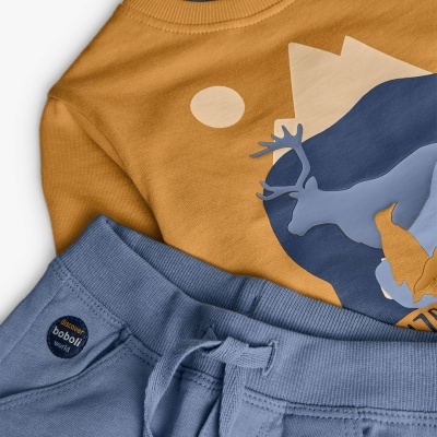 Conjunto de roupa de criança com camisola castanha e calças azuis claras.