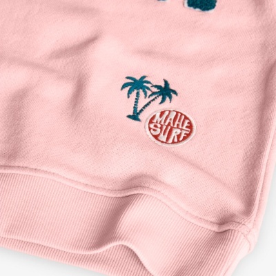 Peça de vestuário rosa com bordado de palmeiras azuis e selo vermelho MAHE SURF