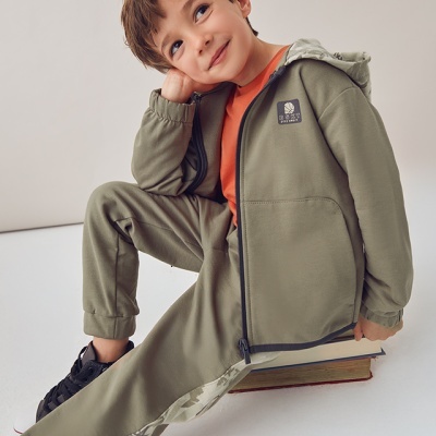 Menino sentado com roupa desportiva verde e t-shirt laranja