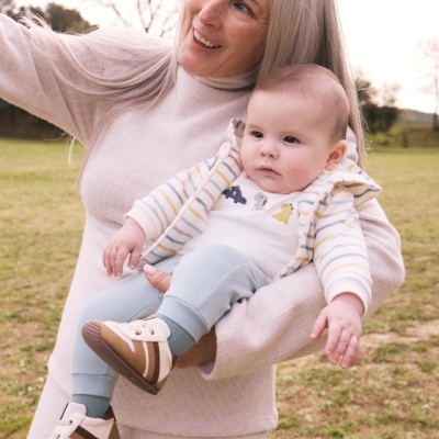 Mulher com bebé vestido com casaco às riscas e sapatilhas castanhas e brancas num parque ao ar livre