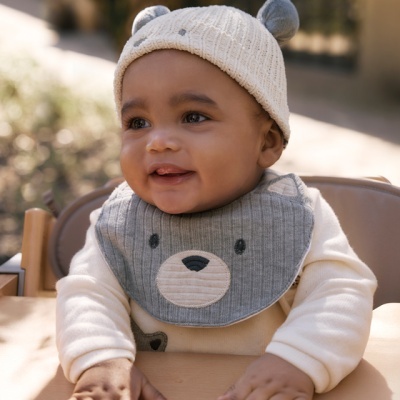 Bebé com gorro e babete de urso sentado em cadeira alta de madeira