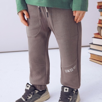 Calças castanhas de criança com calçado desportivo cinzento e branco ao lado de livros.