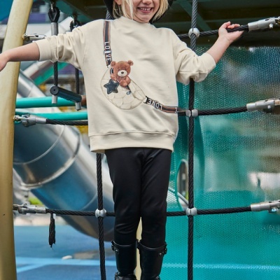 Menina com casaco bege e calças pretas numa estrutura de parque infantil