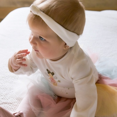 Bebé com roupa colorida e faixa branca na cabeça sentada num quarto