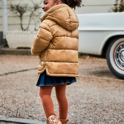 Menina de costas com casaco acolchoado castanho claro e vestido azul escuro na rua junto a carro clássico branco