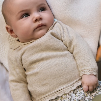 Bebé com camisola bege de malha e saia floral deitada sobre tecido branco