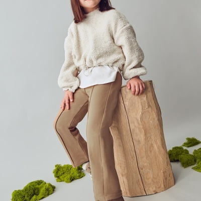 Criança vestindo roupas casuais e sapatilhas, posando junto a um tronco de madeira em estúdio com musgo no chão