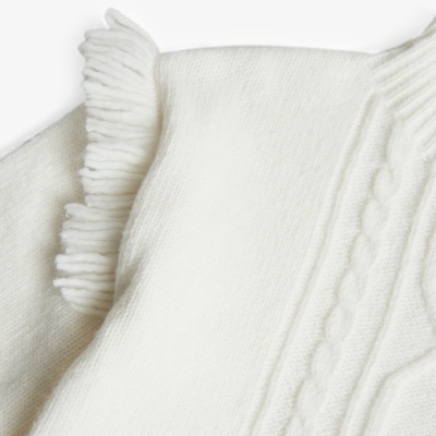 Roupa de malha branca com padrão de tranças e franjas na gola