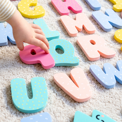 Letras de madeira coloridas com padrões pontilhados sobre tapete cinzento, mão de criança tocando letra Q