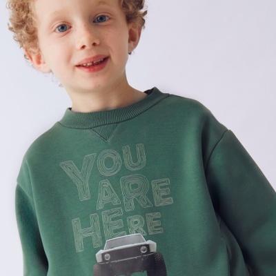 Menino com casaco verde com texto e imagem de carro