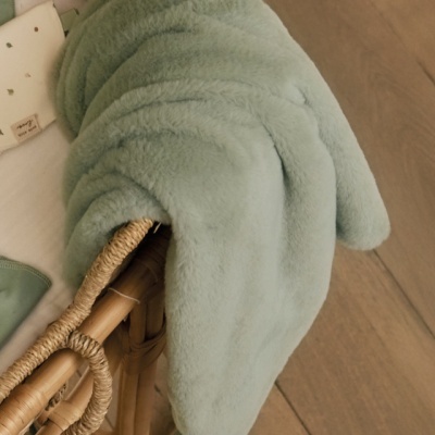 Cobertor verde-água felpudo sobre cadeira de vime em chão de madeira