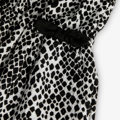 Tecido branco com padrão de manchas pretas e laço preto